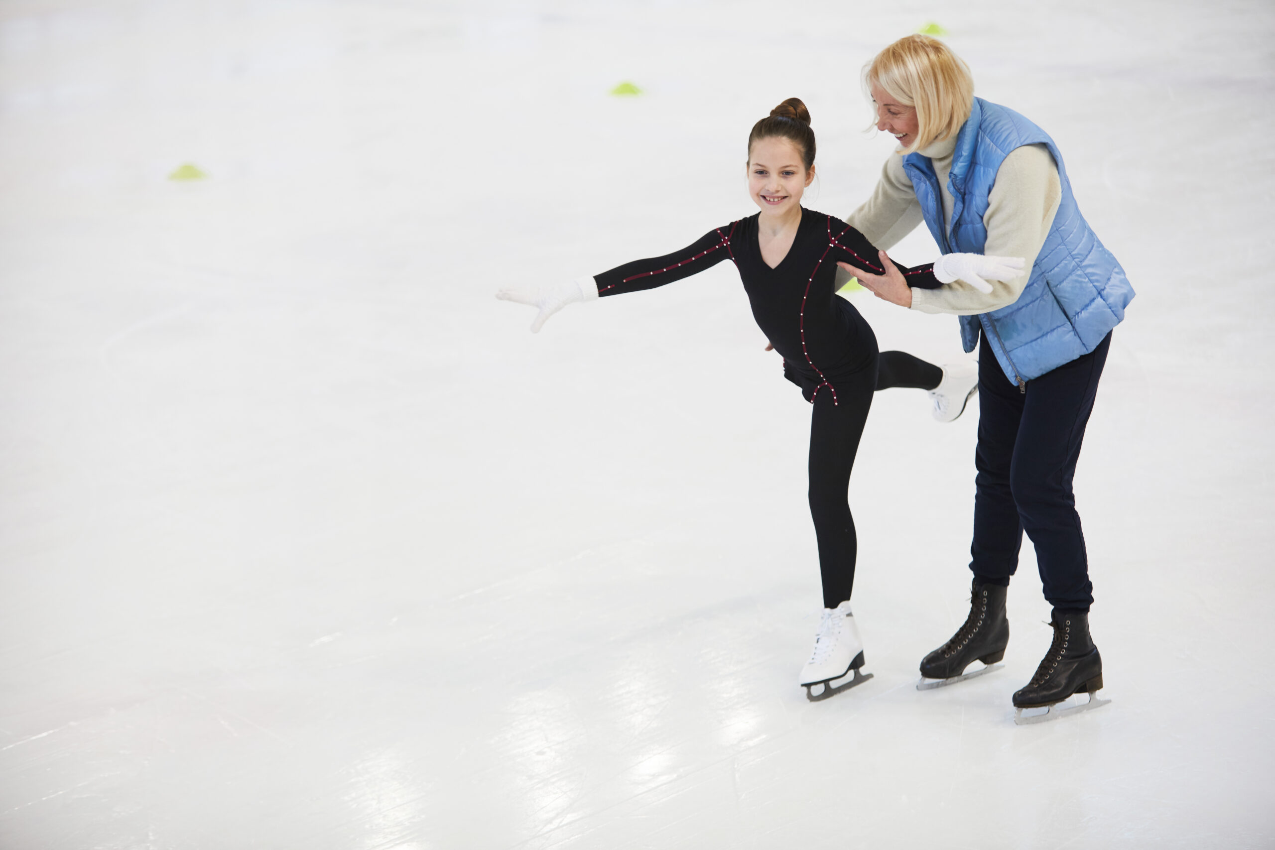 Full length portrait of senior coach helping little girl figure skating on rink, copy space